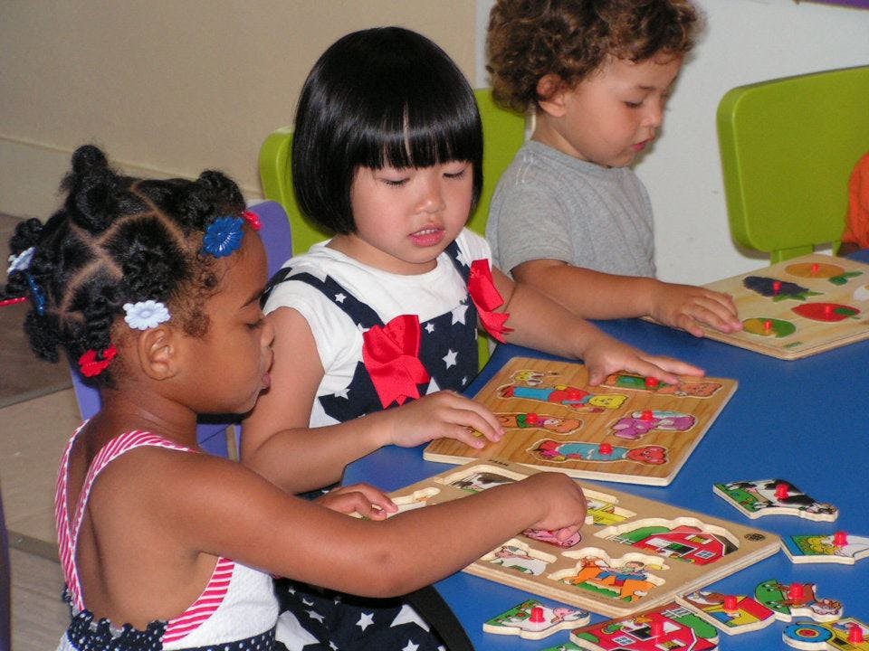 Three children playing with wooden puzzles at a table