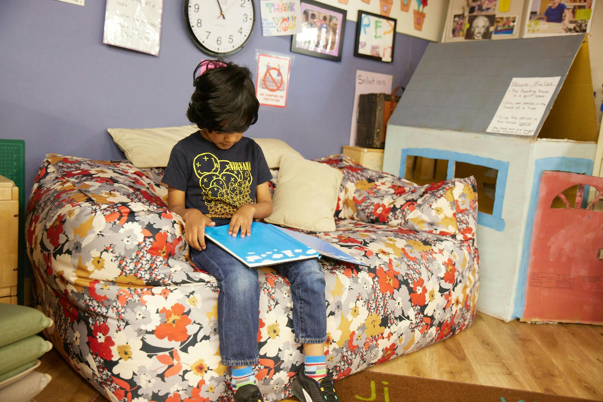 Child sitting on a floral couch reading a book in a classroom