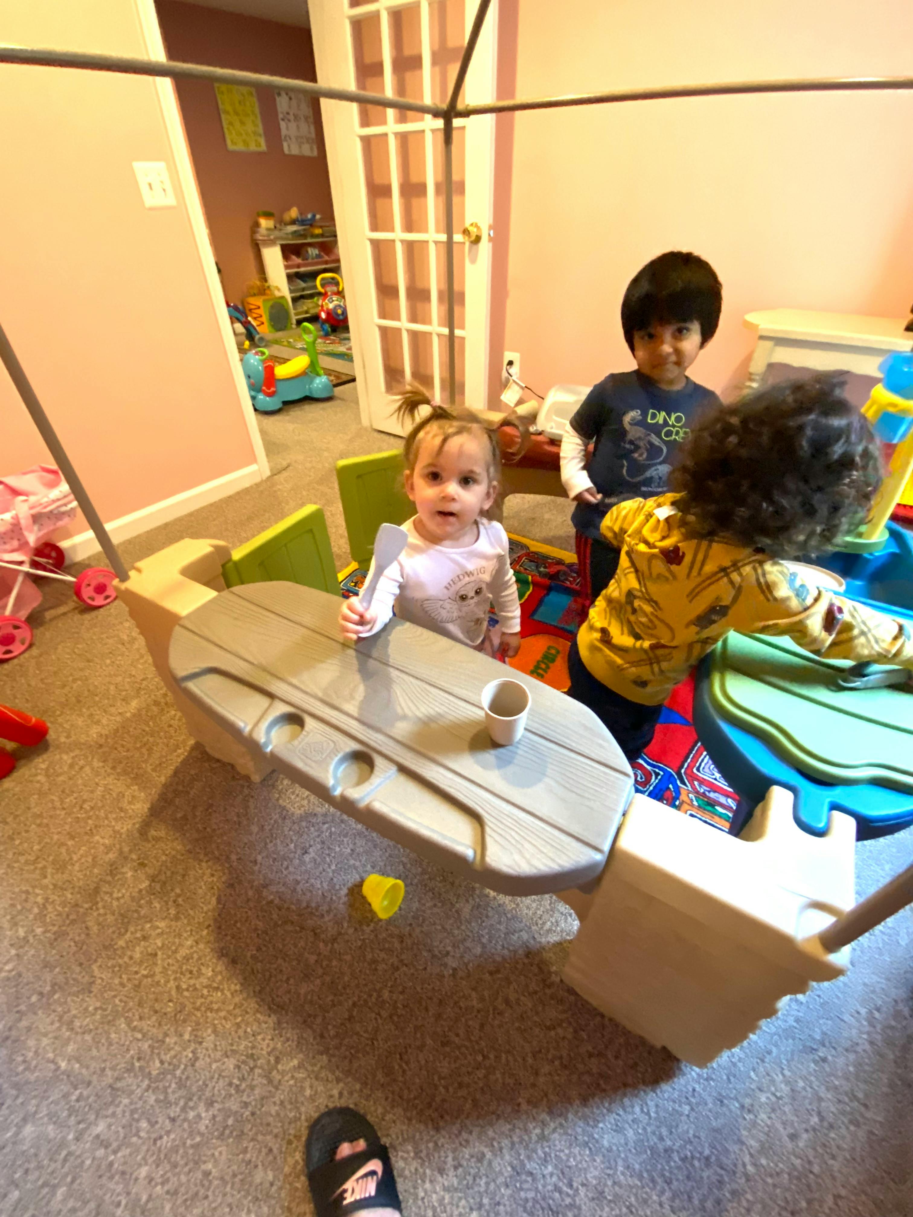 Three children playing with a toy table and other toys in a room