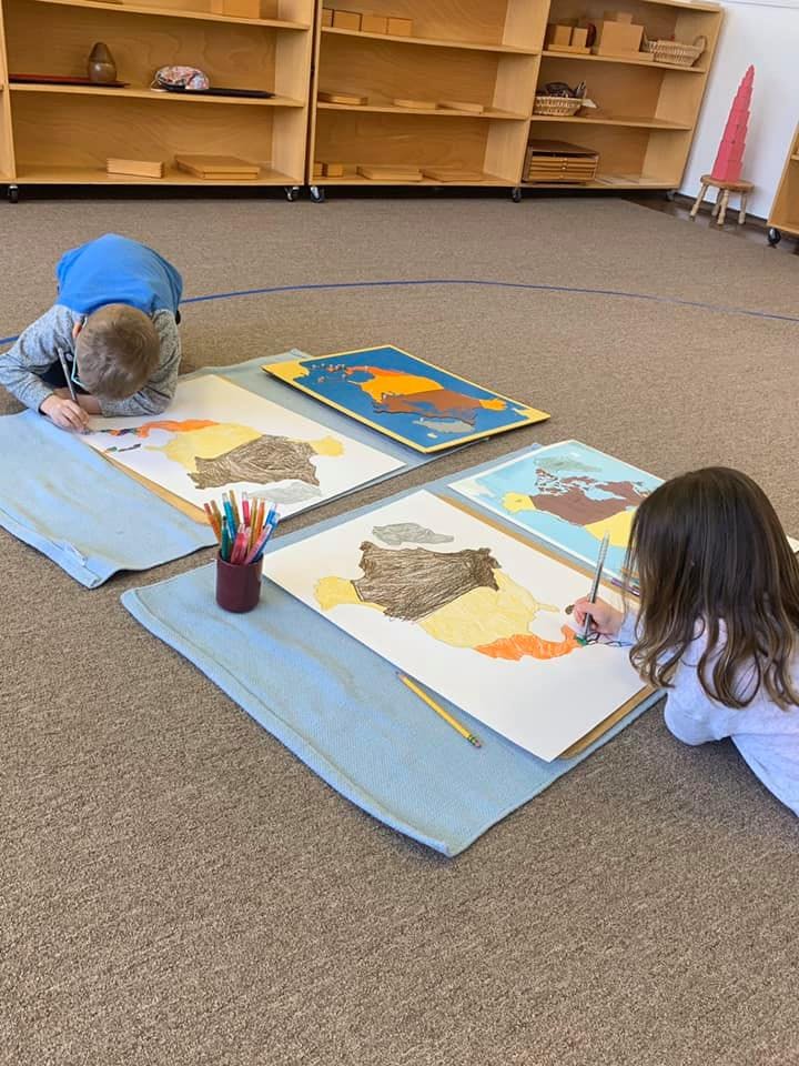 Two children lying on the floor drawing and painting