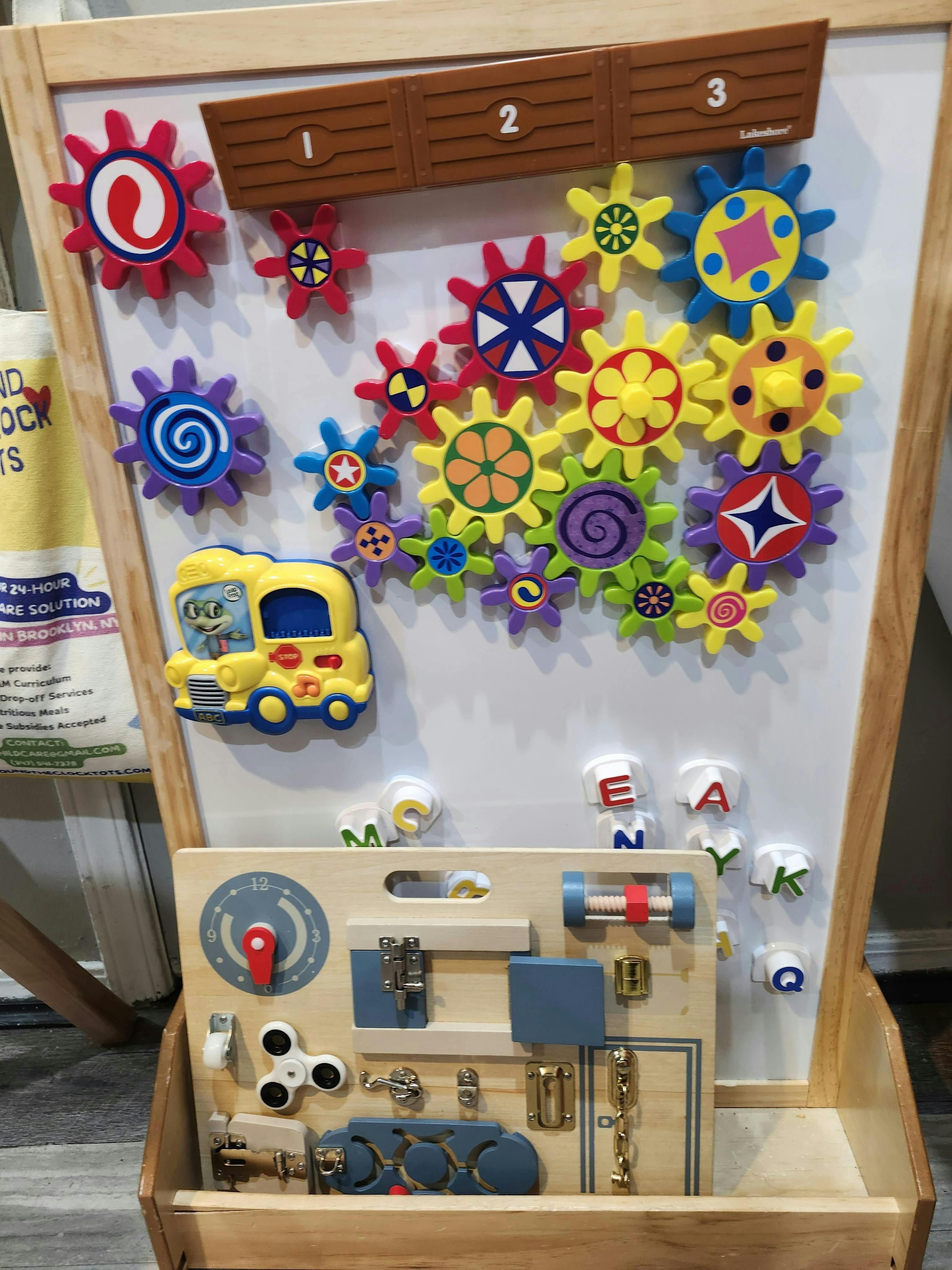 Whiteboard with colorful magnetic gears, a yellow bus, and a wooden activity board