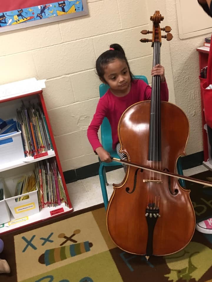 Child sitting on a chair holding a cello and bow