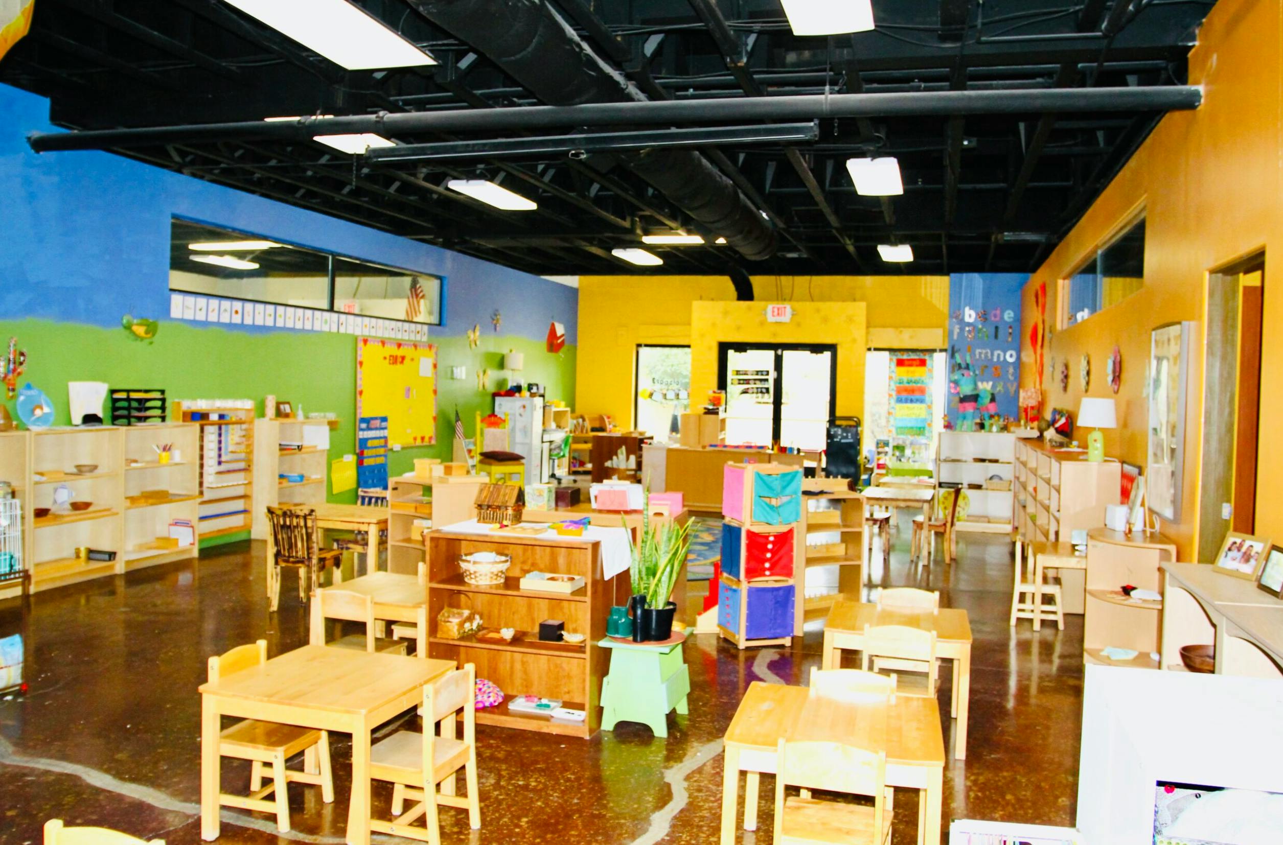 Classroom with small tables and chairs, shelves with learning materials