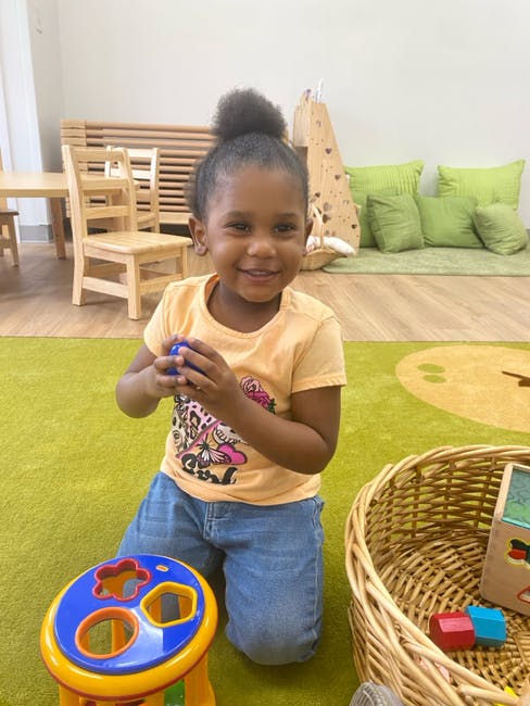Child kneeling on a rug holding a small blue ball