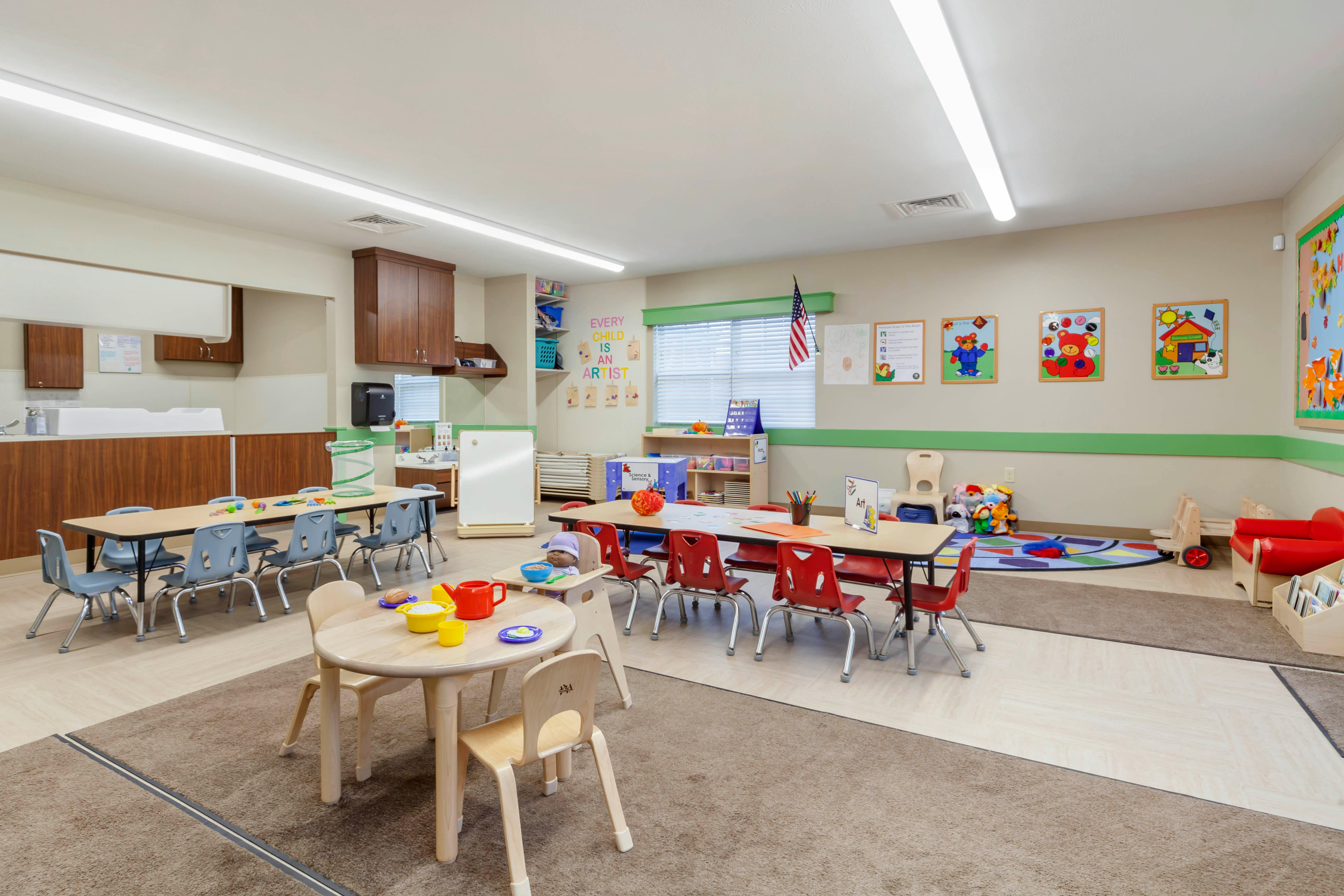 An empty early childhood classroom with small tables, chairs, and play areas