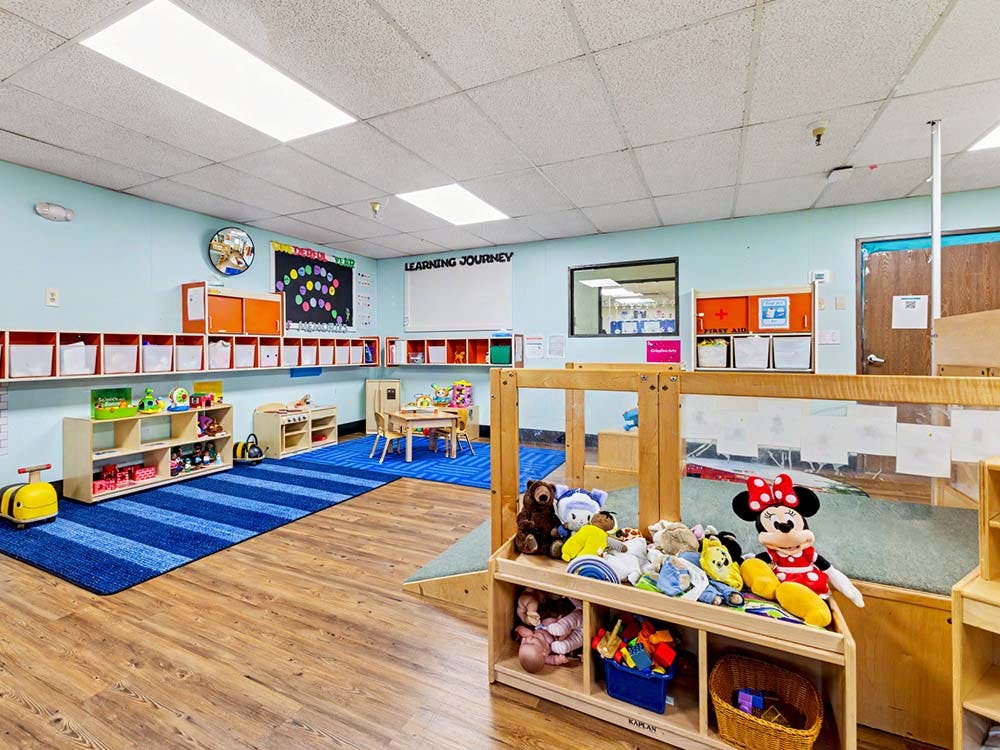 Learning center classroom with blue striped rug, small tables, and shelves of toys