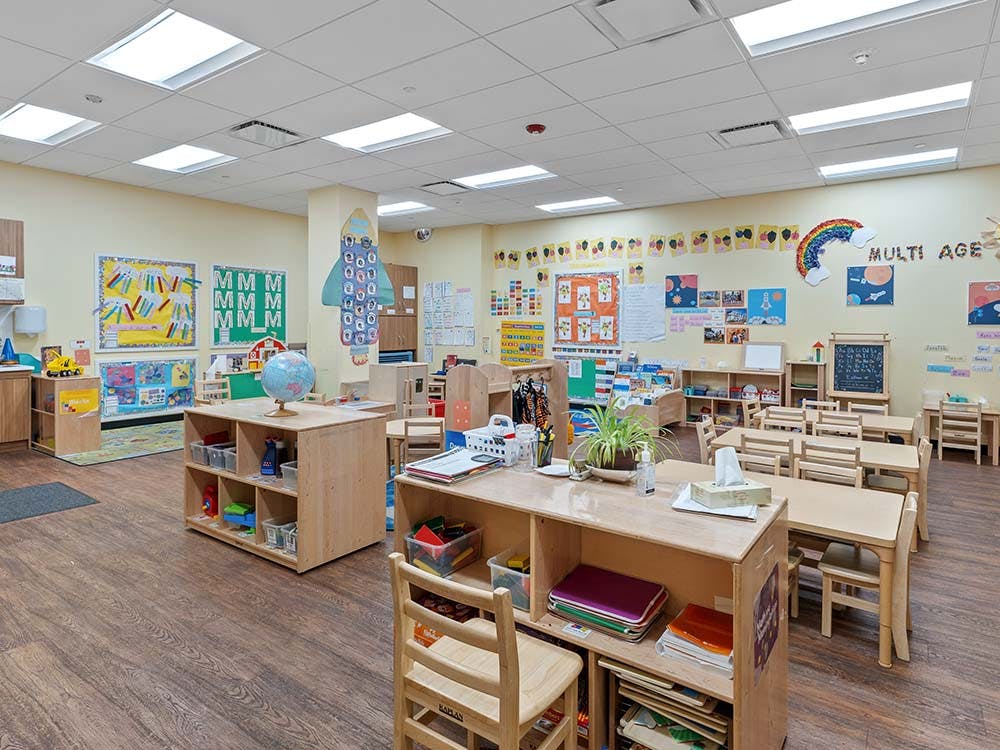 Empty preschool classroom with small wooden tables and chairs