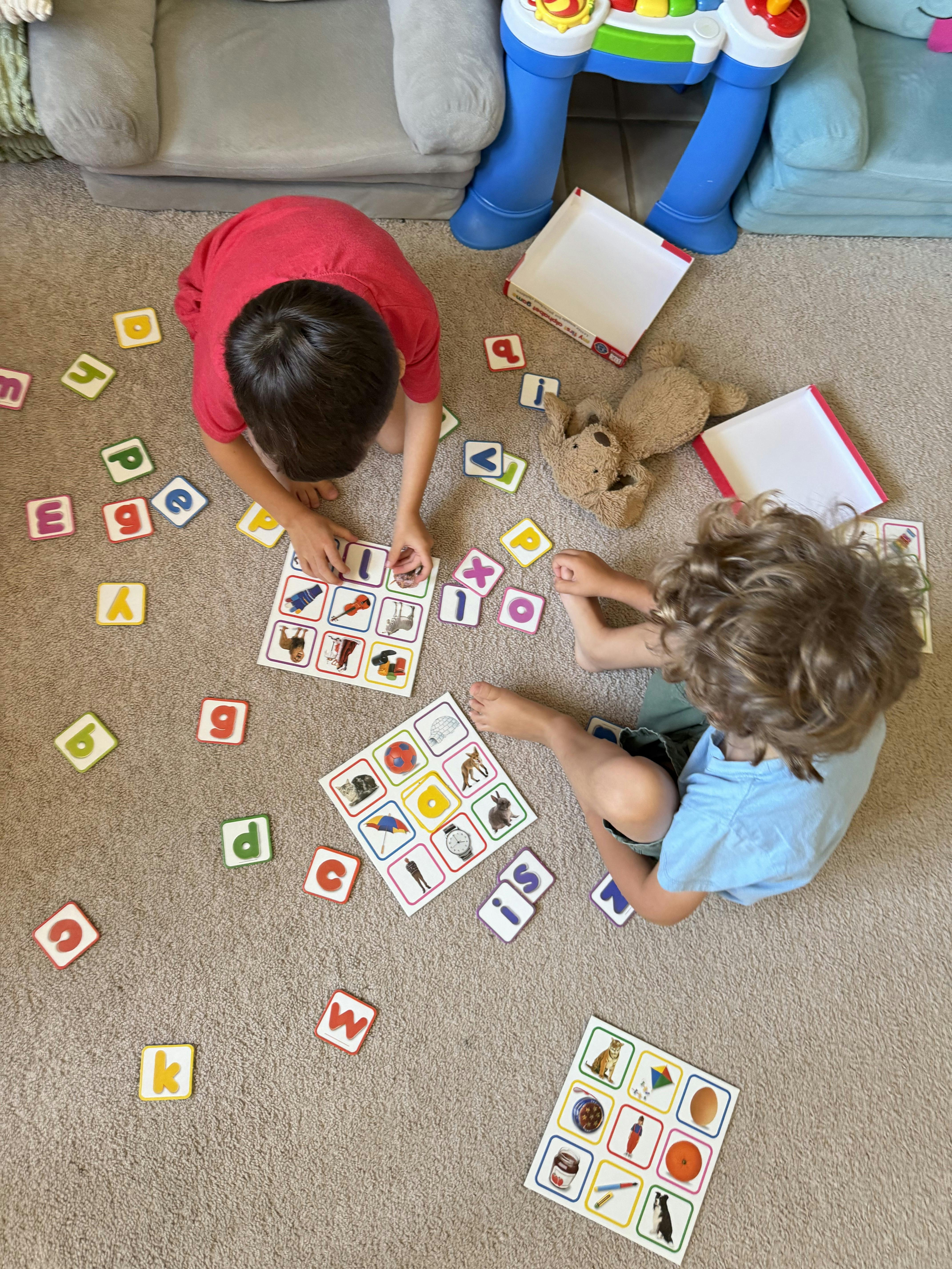 Two children playing with alphabet letter tiles and picture cards on a carpet