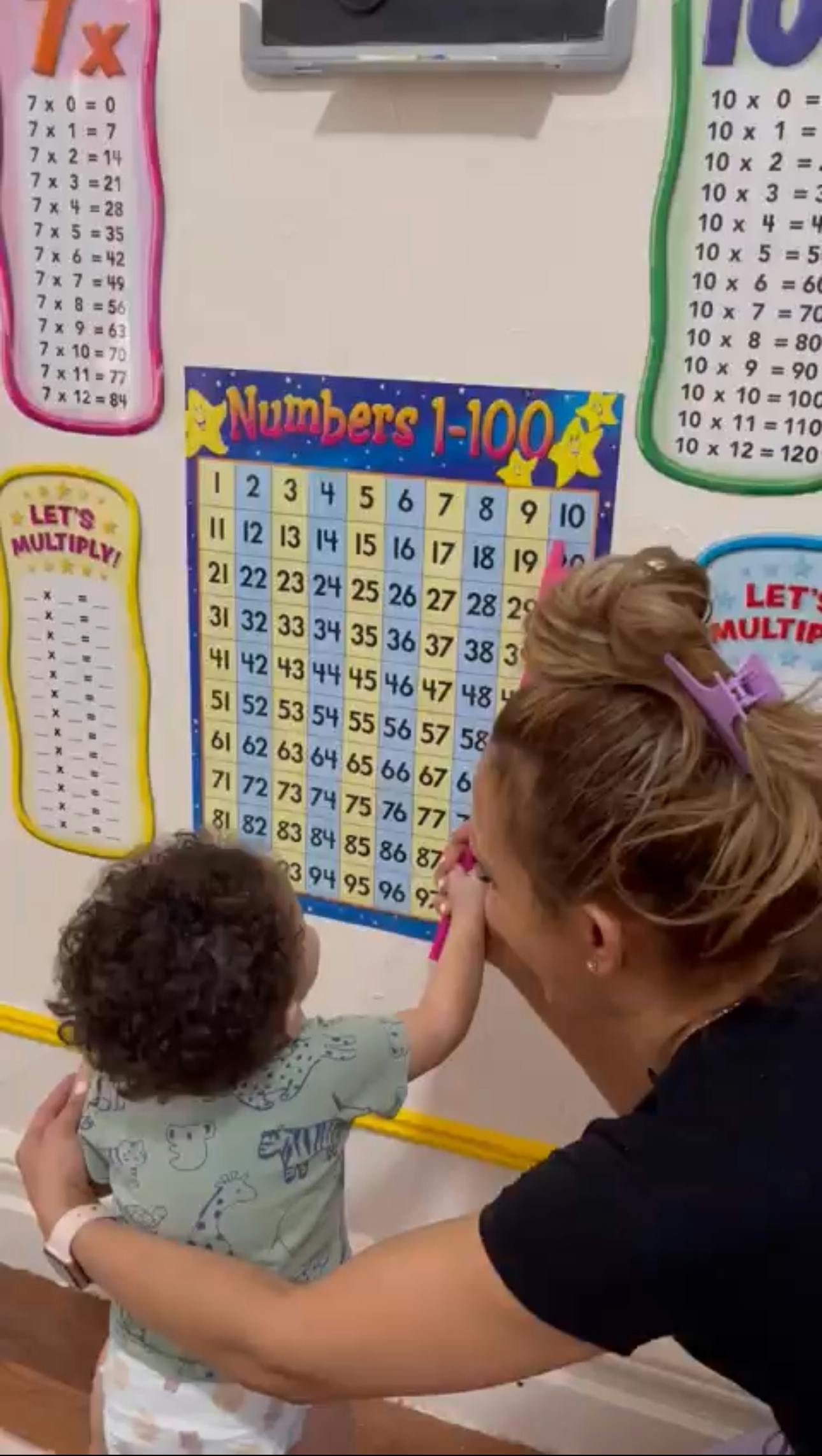 Person helping a child point to a numbers chart