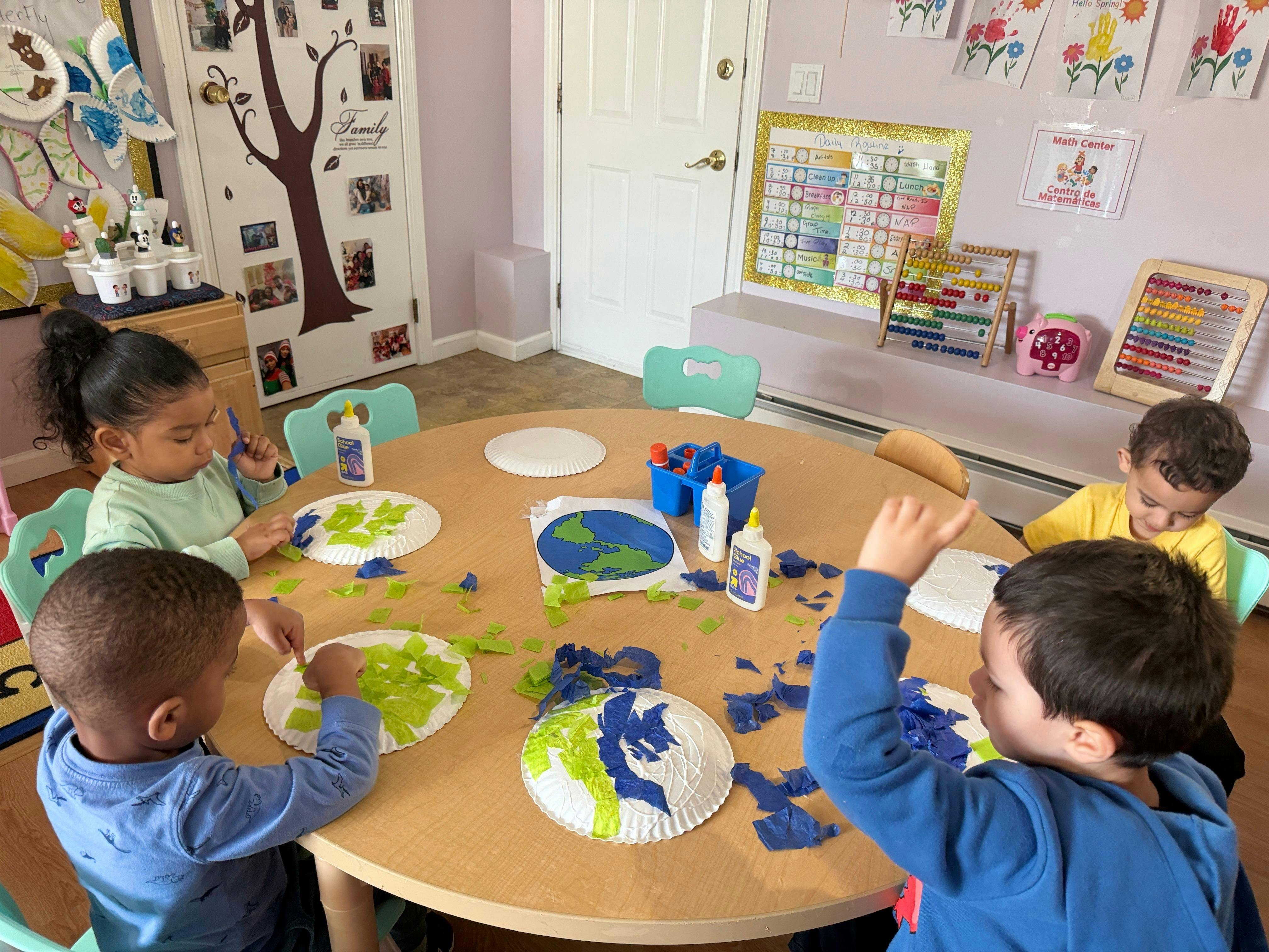 Four children doing a craft activity at a round table in a classroom