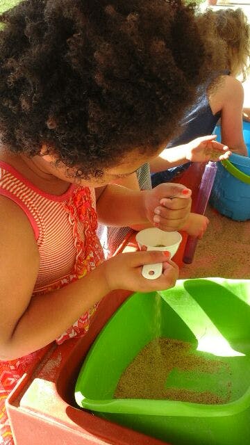Child pouring sand from a funnel into a green container