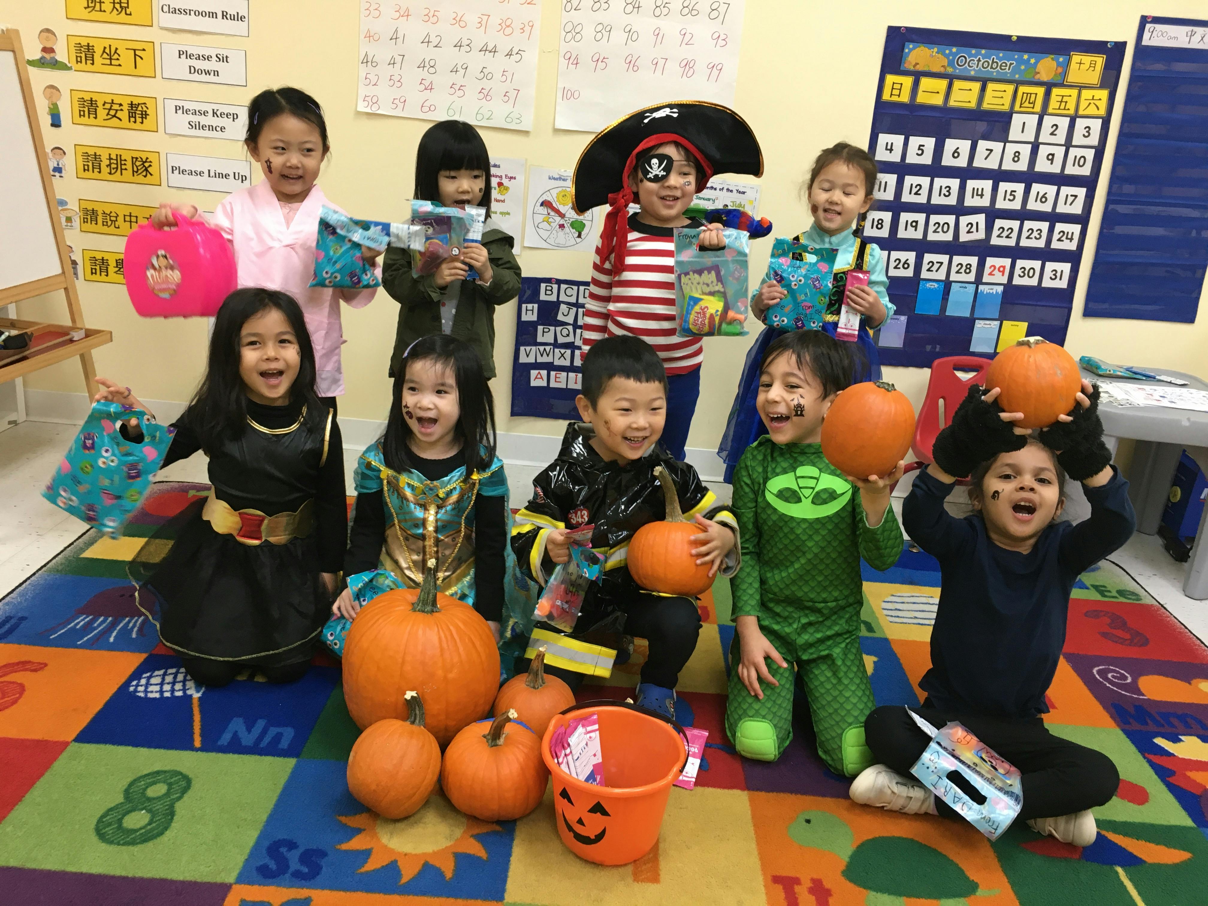 Children in costumes holding pumpkins and treat bags in a classroom