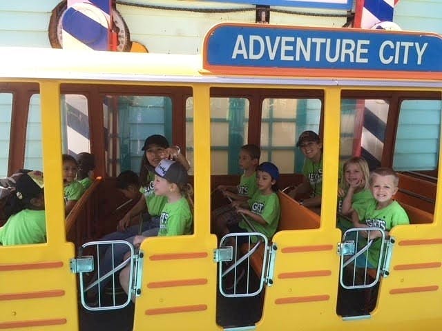 Children and adults riding a yellow train car with "ADVENTURE CITY" sign