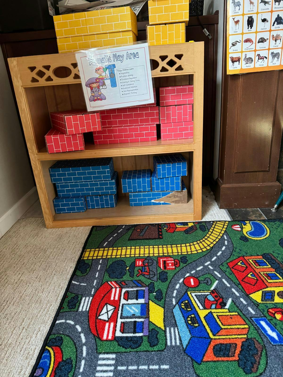 Wooden shelf with red and blue brick-patterned boxes, play rug on road rug