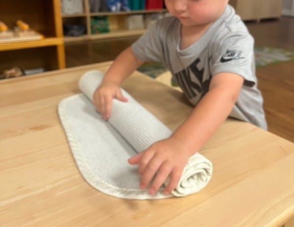 Child rolling up a light-colored mat on a wooden table