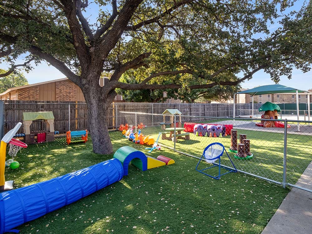 Outdoor playground with a blue tunnel, small playhouses, and artificial grass