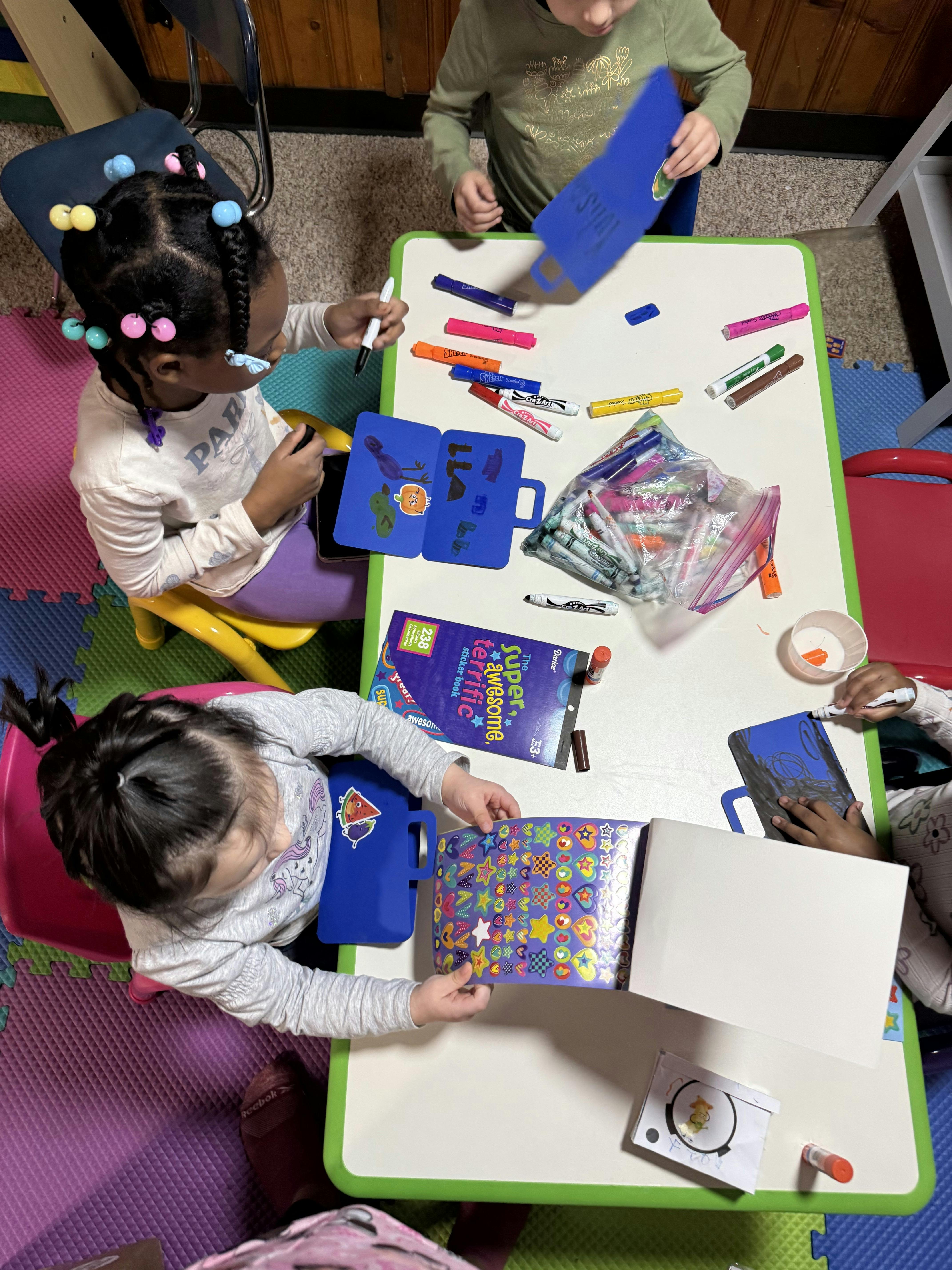 Children drawing and placing stickers at a small table