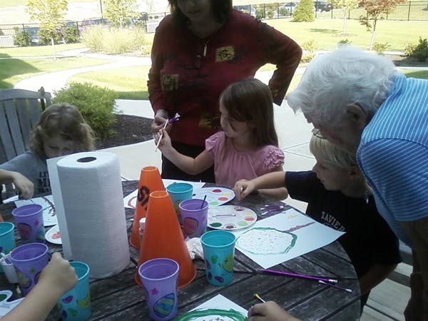Adults and children painting at a table outdoors