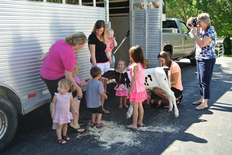 People and children gathered around a calf near a trailer