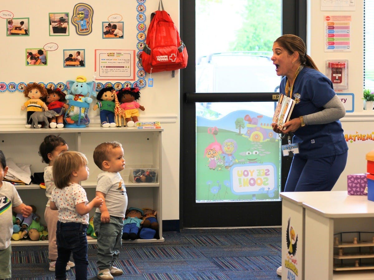 Adult holding books leaning over and speaking to a group of young children