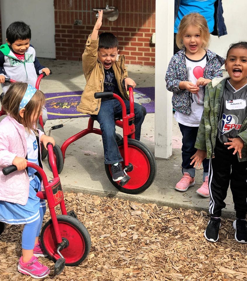 Children playing with red tricycles outdoors