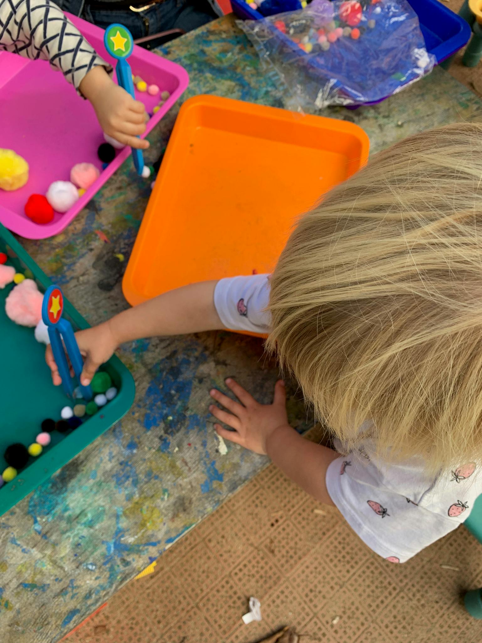 Child playing with pom-poms and tongs