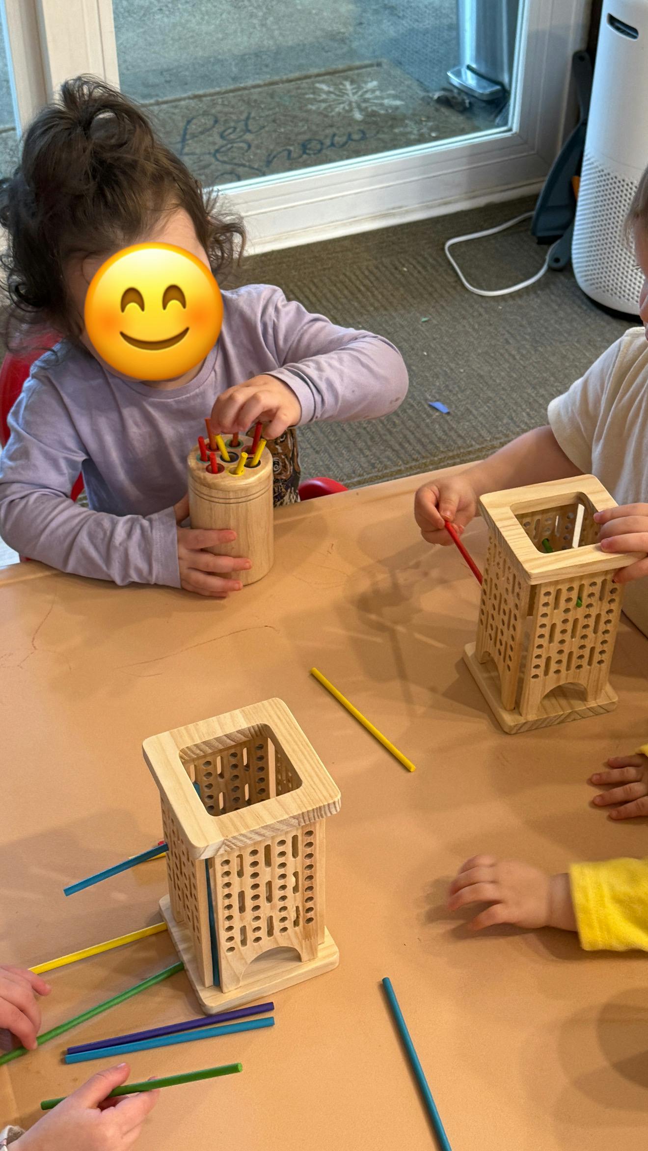 Children playing with wooden stick-insertion toys on a brown table