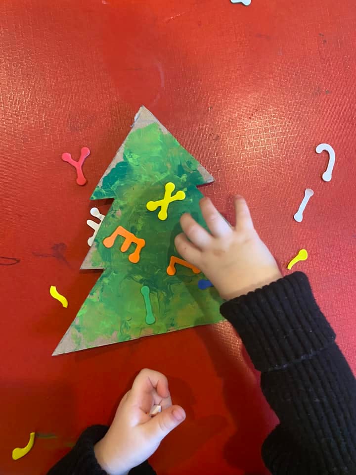 Child's hands decorating a paper Christmas tree with foam letters