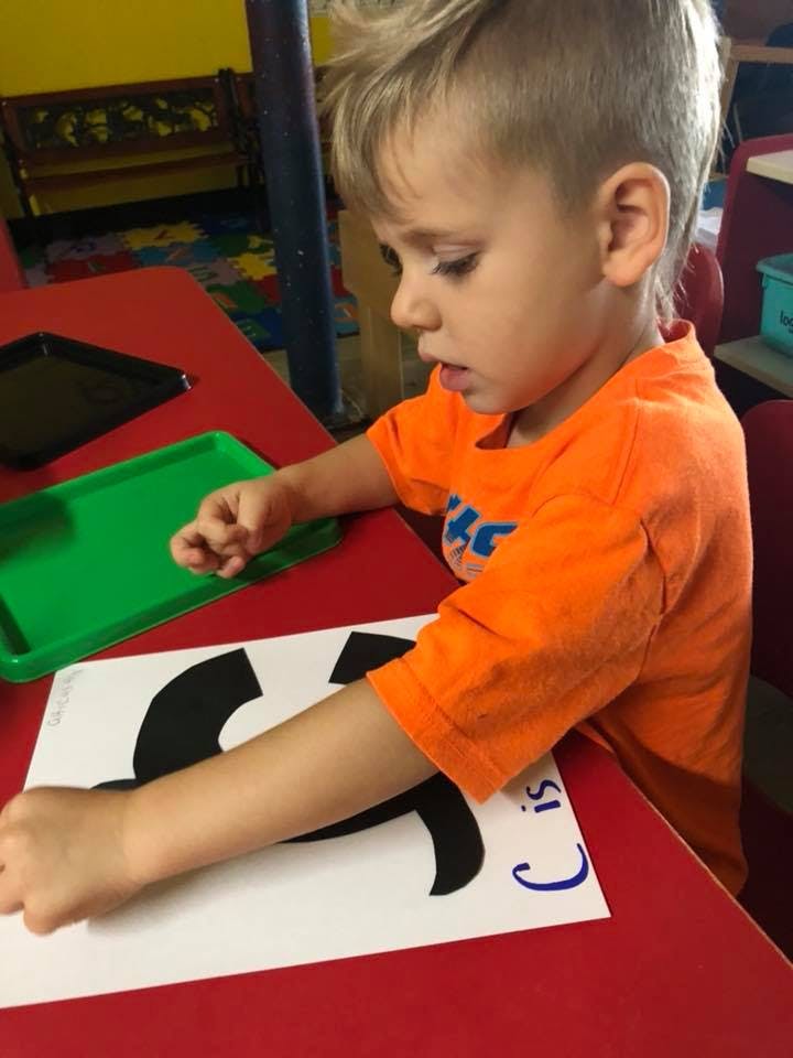 Child at a red table working on a paper with a large black shape