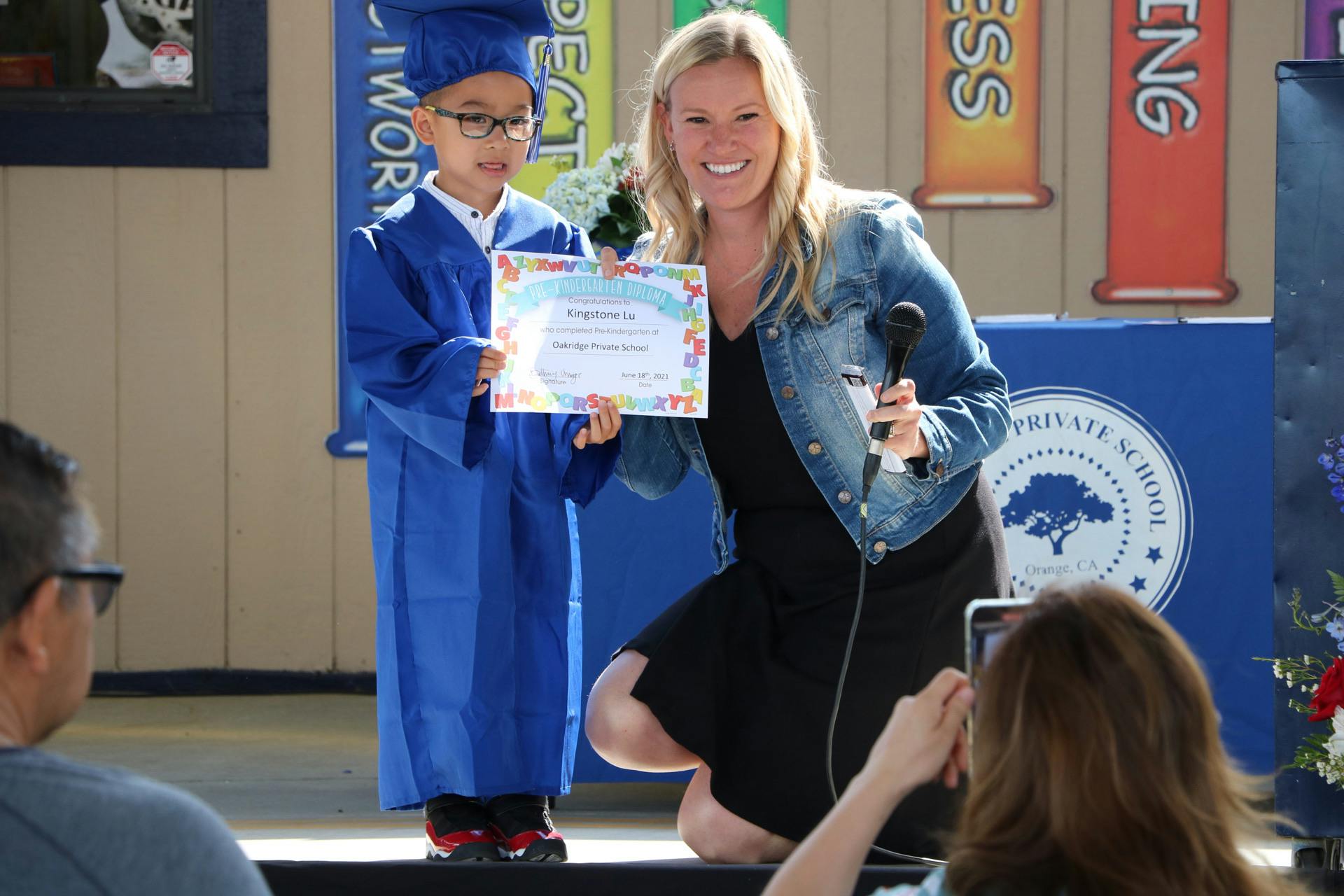 Child in graduation cap and gown holding a certificate with a person kneeling