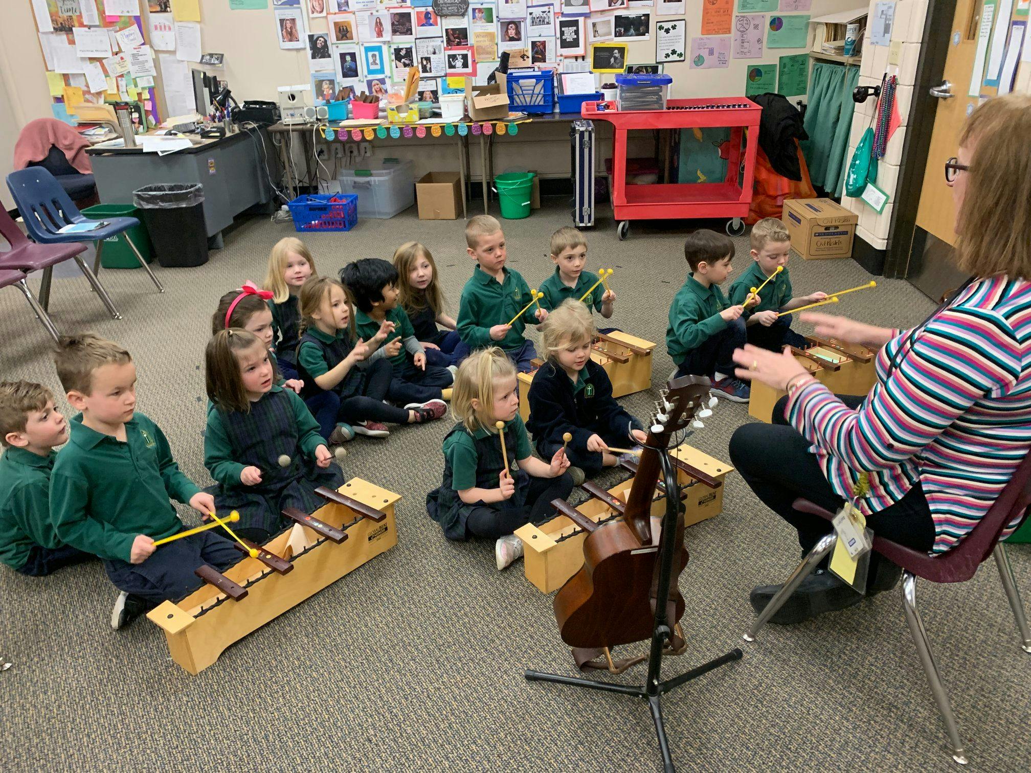 Children playing xylophones in a classroom with an adult