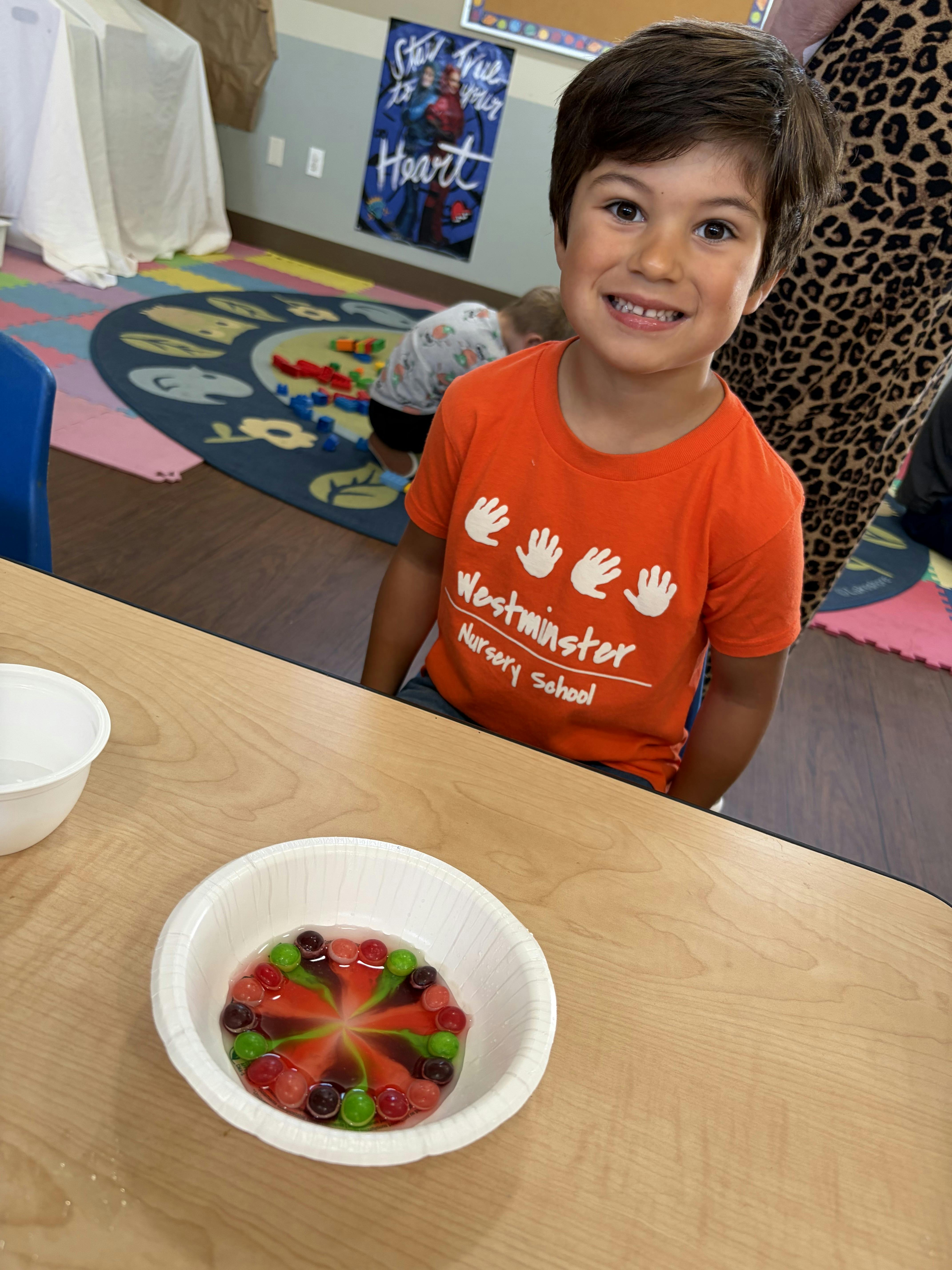 Child in a nursery school t-shirt standing by a table with a bowl of candy