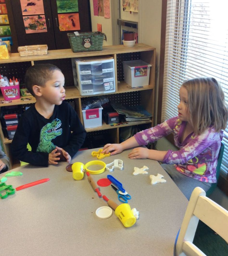 Two children at a table with playdough and tools