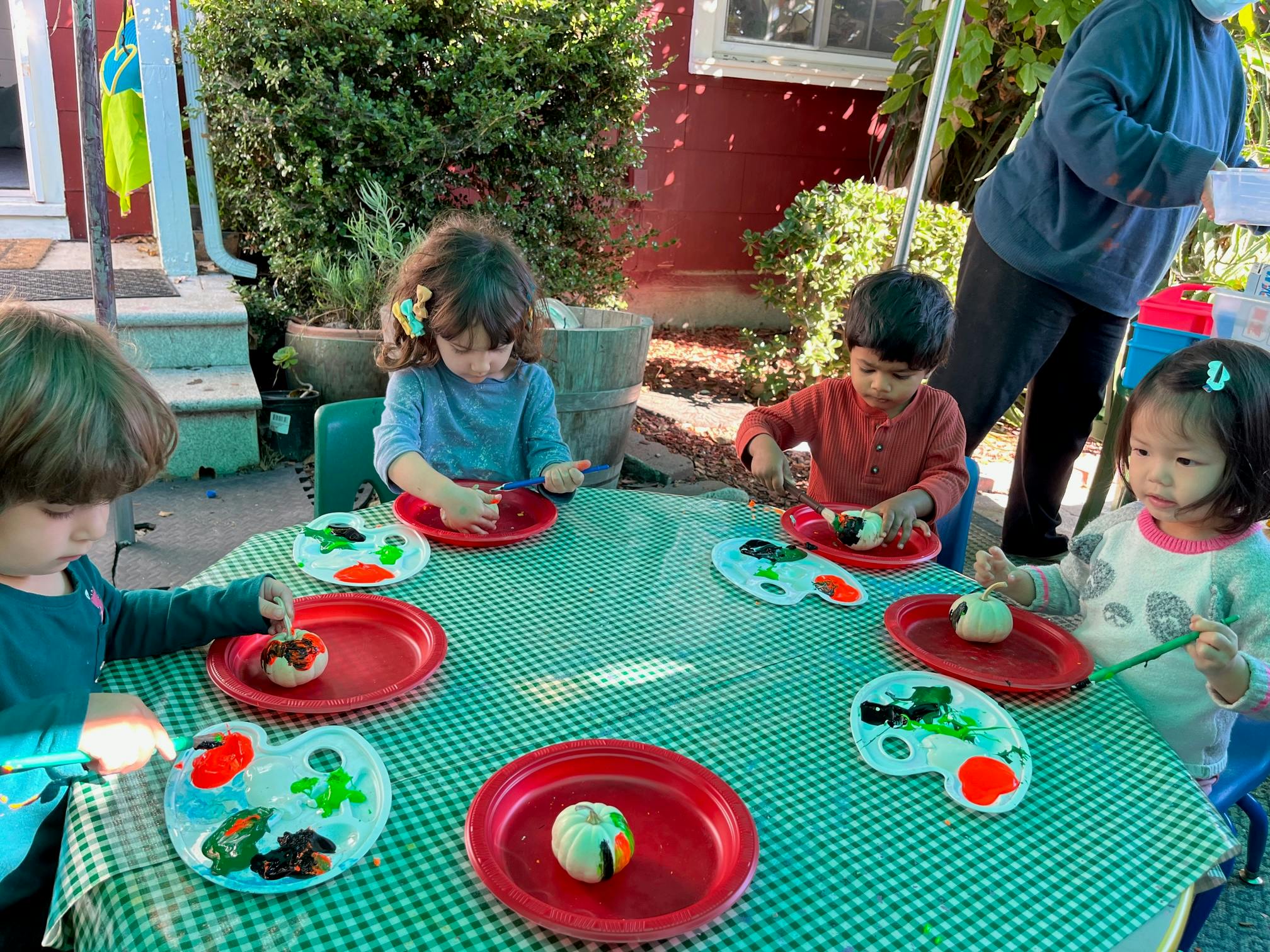 Children painting small objects at a table outdoors