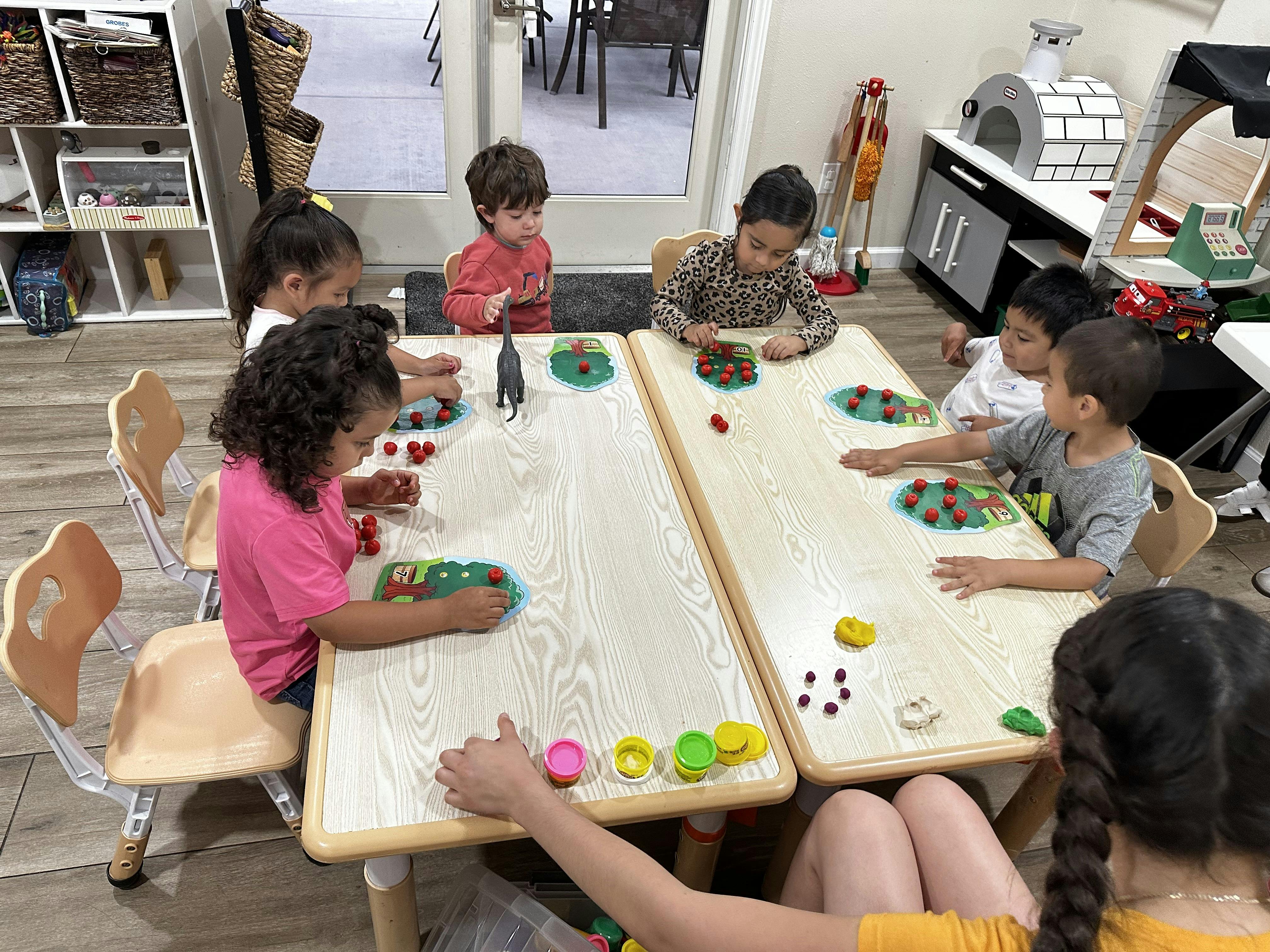 Children playing with toys and play-doh around two light-colored tables