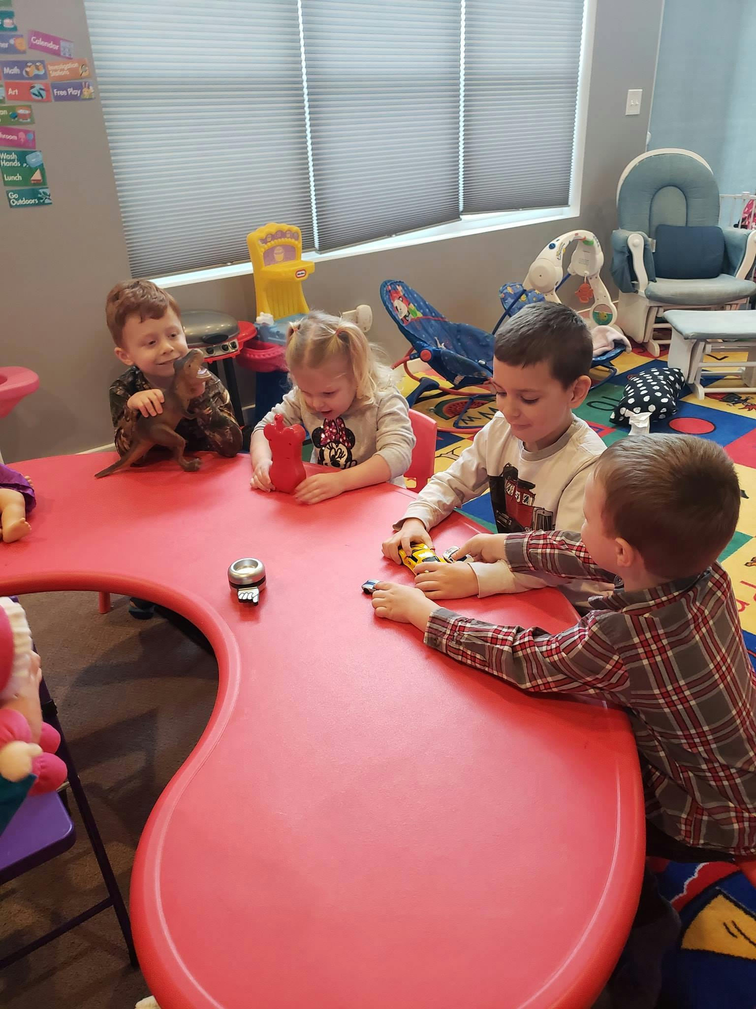 Four children playing with toys at a red table in a classroom