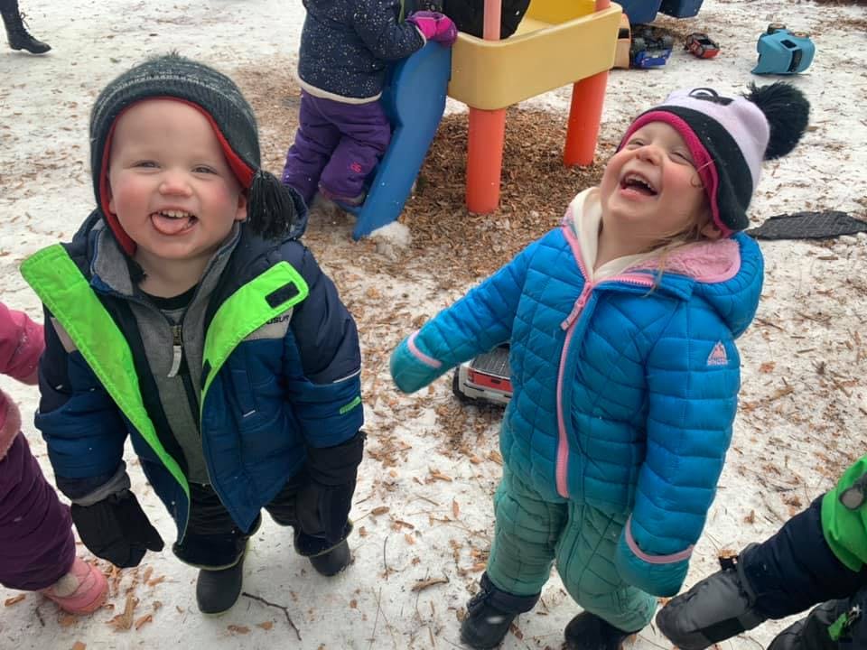 Two children in winter clothing playing in snow