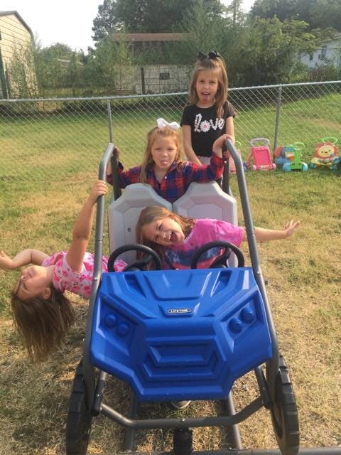 Three children playing on and around a blue toy car