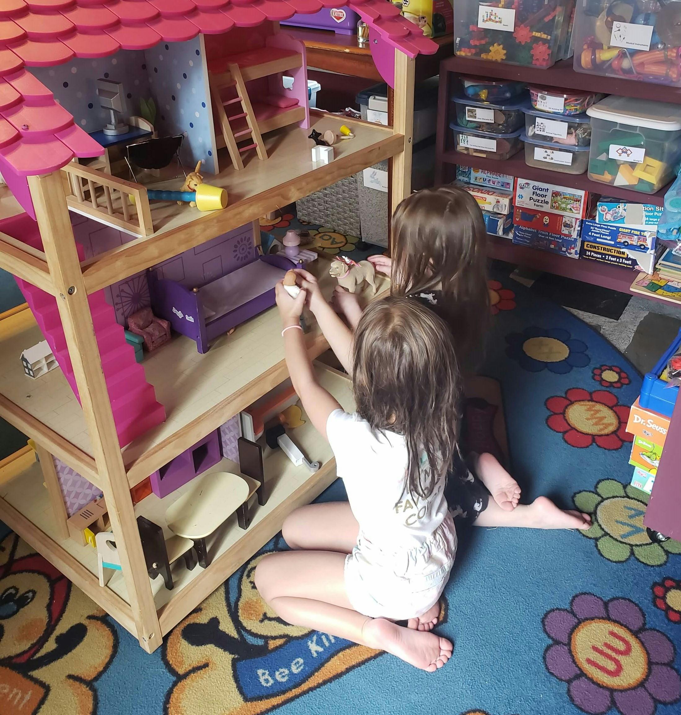 Two children playing with a dollhouse on a dollhouse