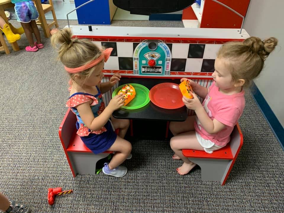 Two children sitting at a play diner booth with toy food