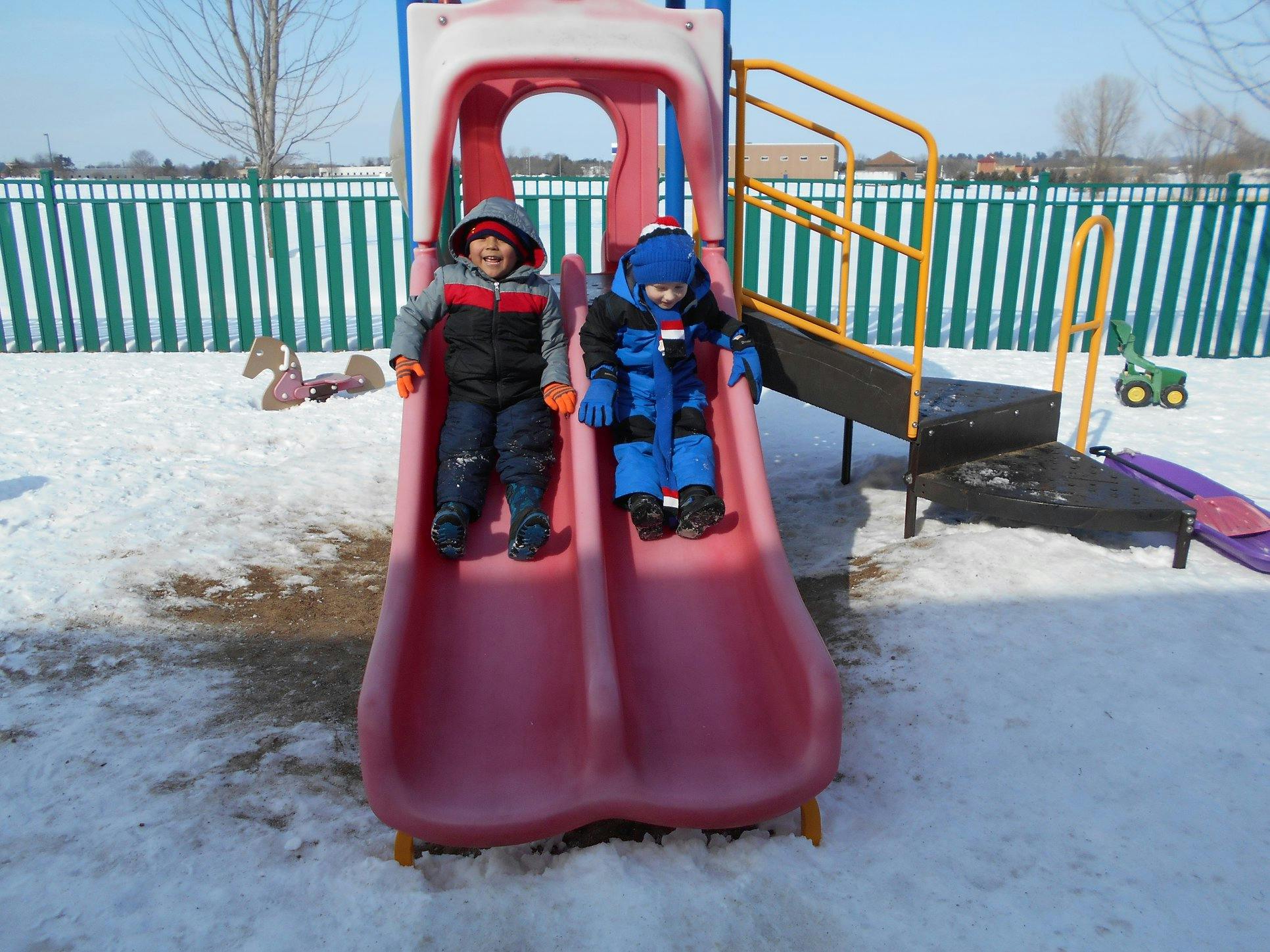 Two children on a red playground slide in the snow
