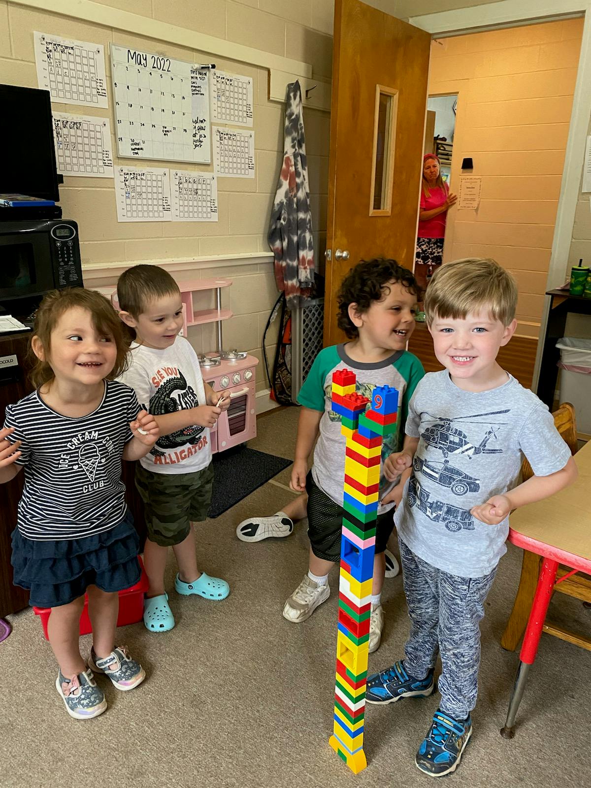 Three children standing around a tall tower of colorful building blocks