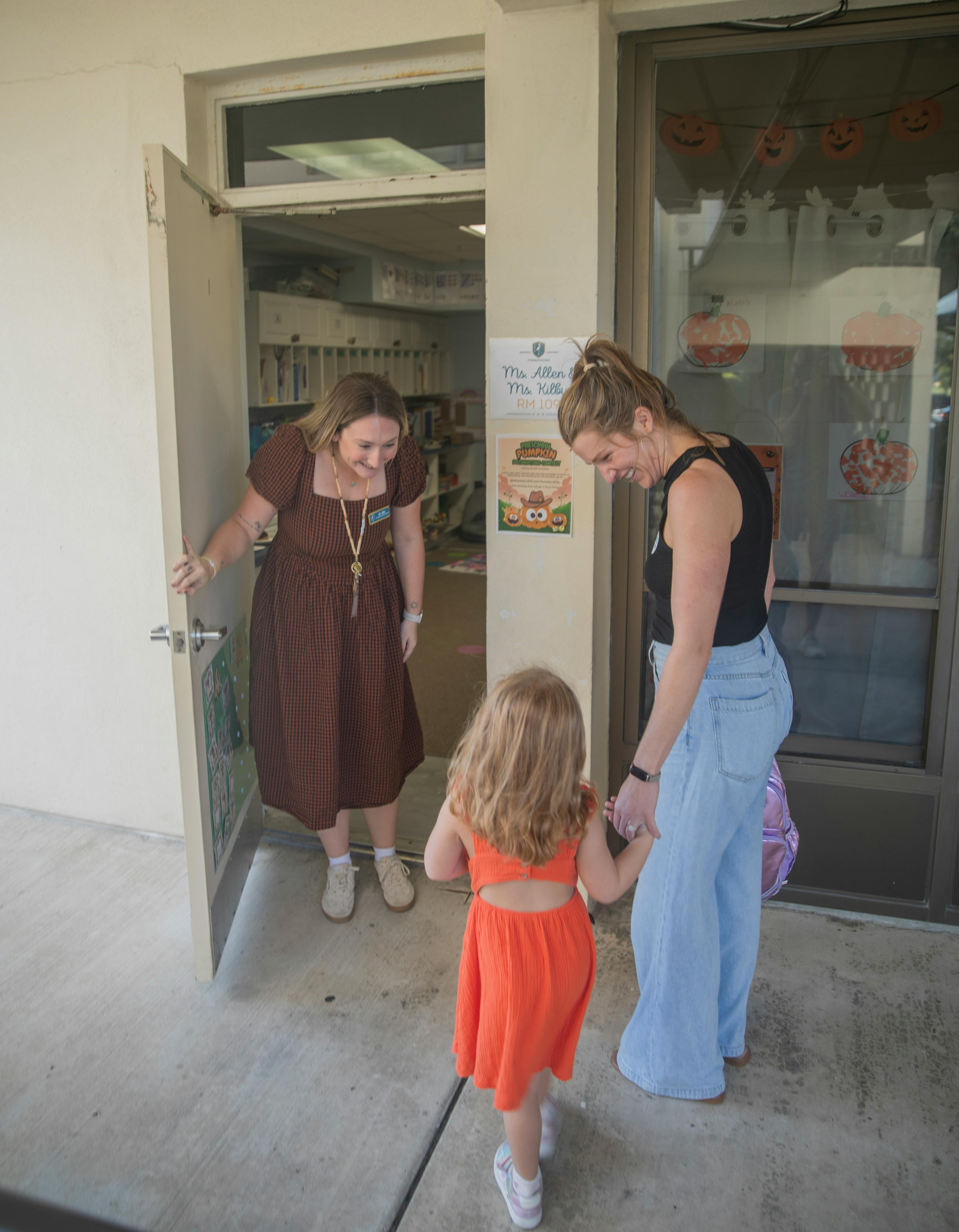 Adult opening a classroom door for a person holding a child's hand