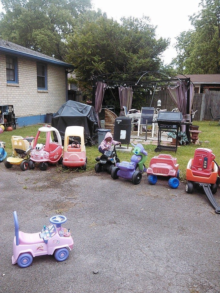 Child on a ride-on toy surrounded by other ride-on toys in a yard
