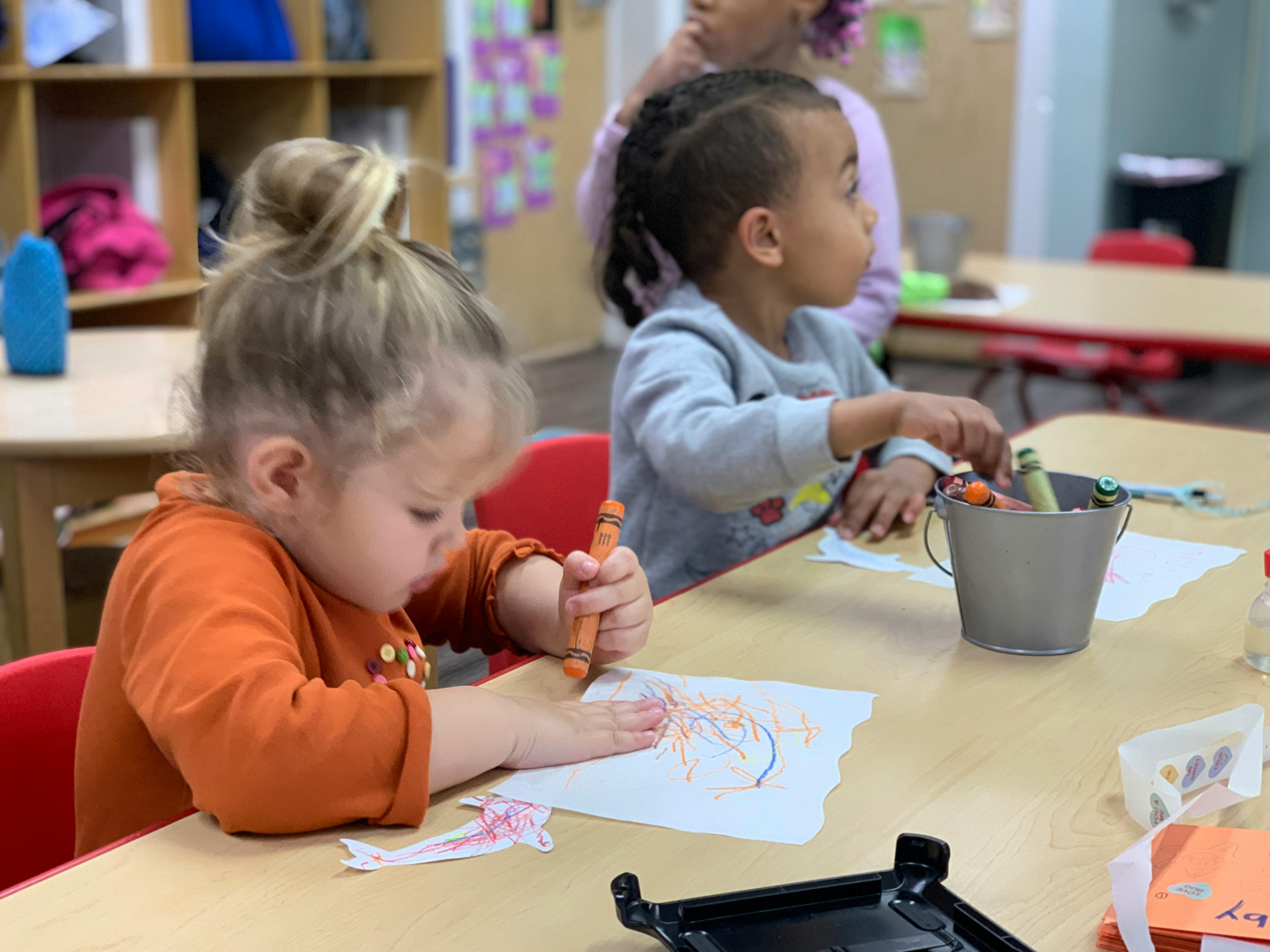 Child drawing with a crayon at a table in a classroom