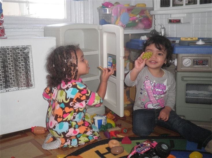 Two children playing with a toy refrigerator