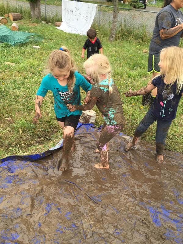 Three children playing in mud on a blue tarp