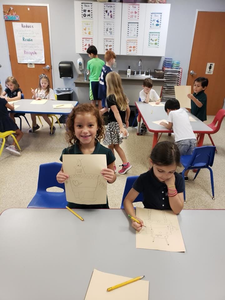 Child holding up a drawing in a classroom with other children