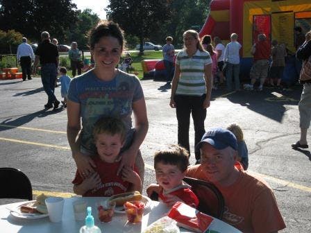 Person standing behind a child, another child and person seated at a table