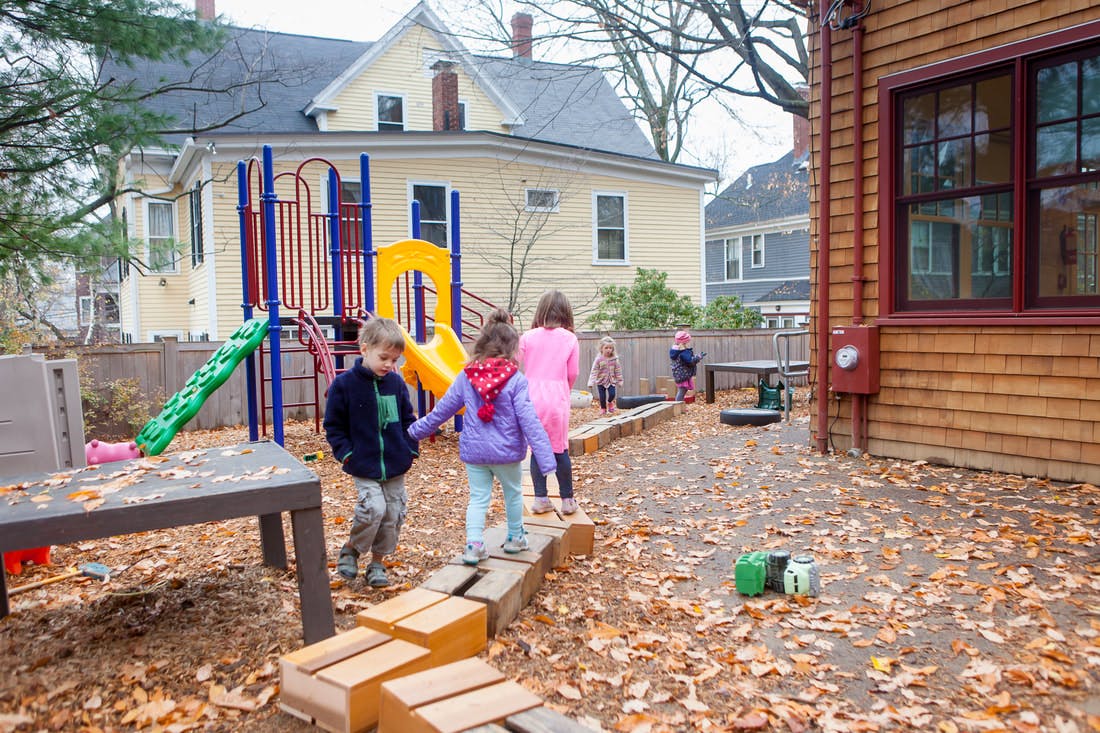 Children walking on wooden blocks in a playground with a slide and house